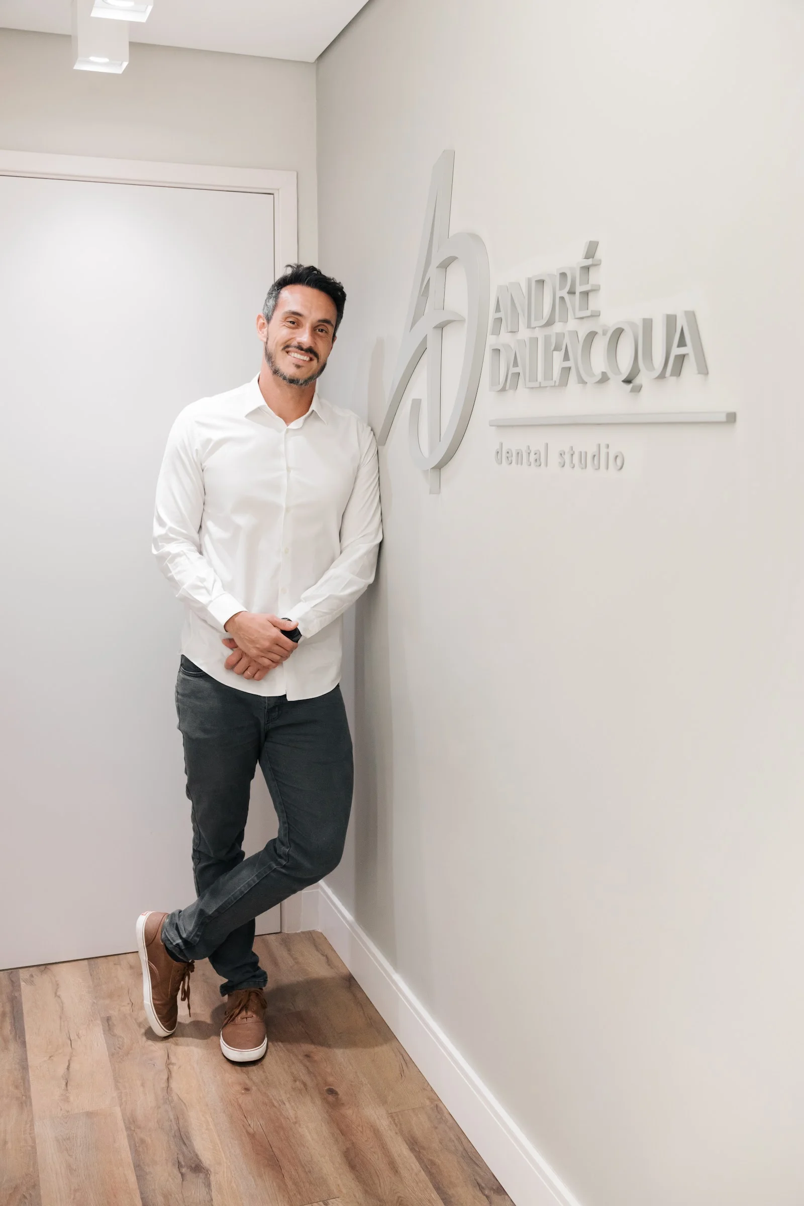 Dr. André Dall’Acqua em frente ao letreiro do consultório, com o monograma AD