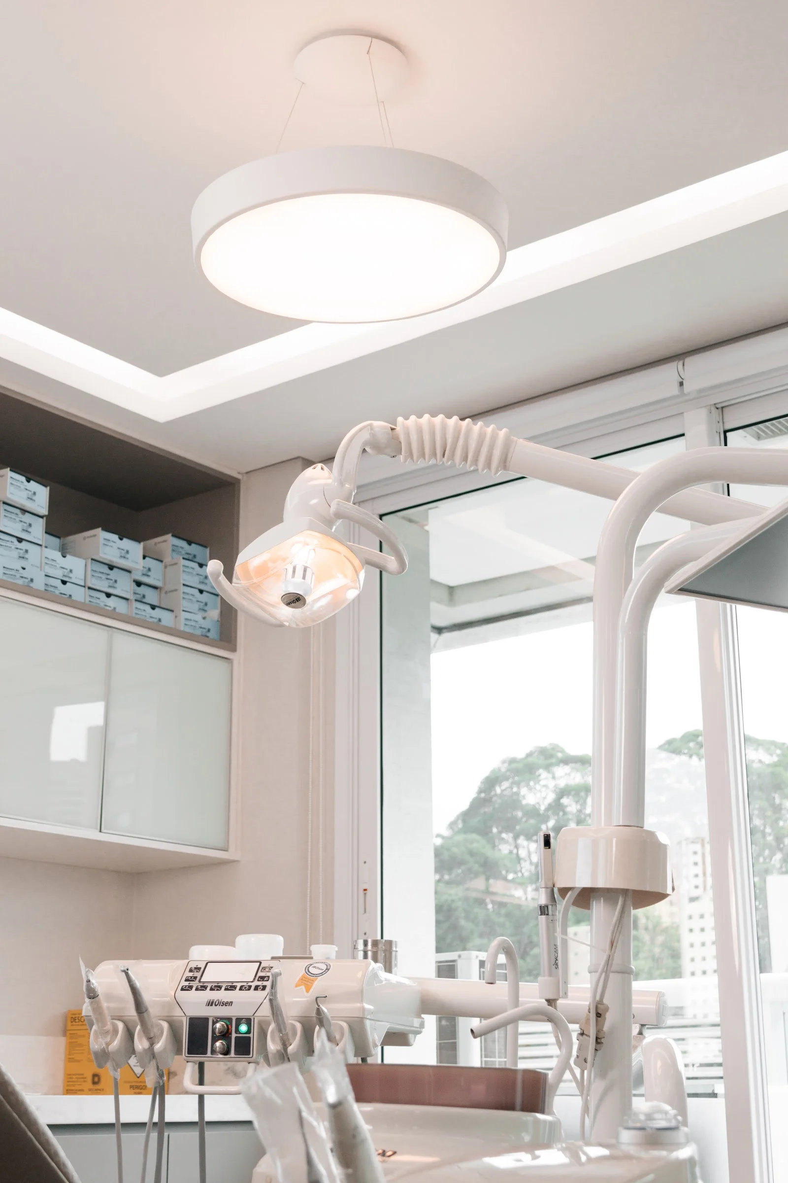Cadeira odontológica, refletor e luminária branca no consultório
